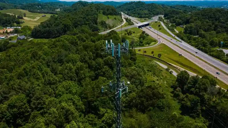 Drone terbang menginspeksi menara telekomunikasi tinggi dengan latar belakang langit biru