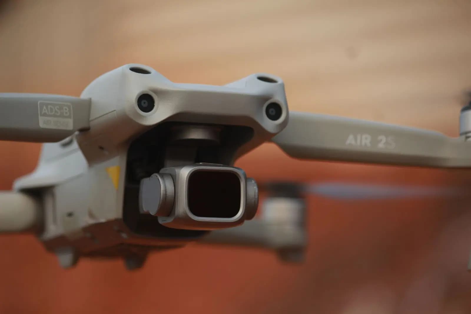 Tangan memegang drone di dekat layar yang menampilkan spesifikasi kamera