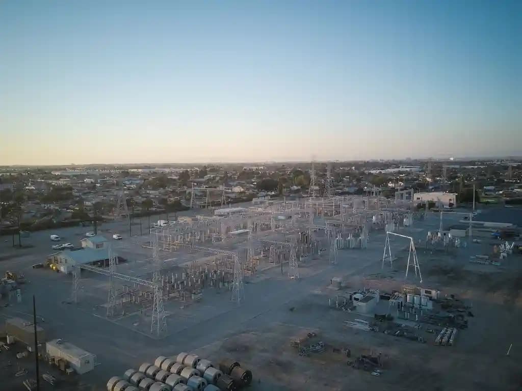 Drone industri terbang di dekat menara transmisi listrik, melakukan inspeksi infrastruktur.