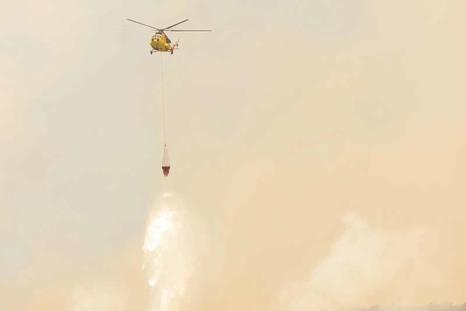 Helikopter pengebom air menjatuhkan air di atas hutan yang terbakar dan berasap tebal