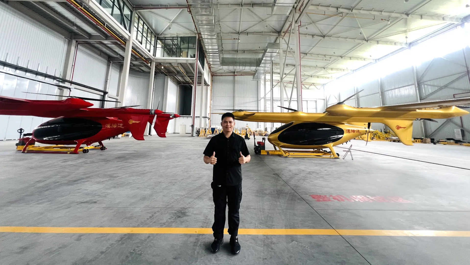 Liu Purnomo di hanggar produksi eVTOL bersama dua purwarupa pesawat listrik lepas landas dan mendarat vertikal berwarna merah dan emas di China